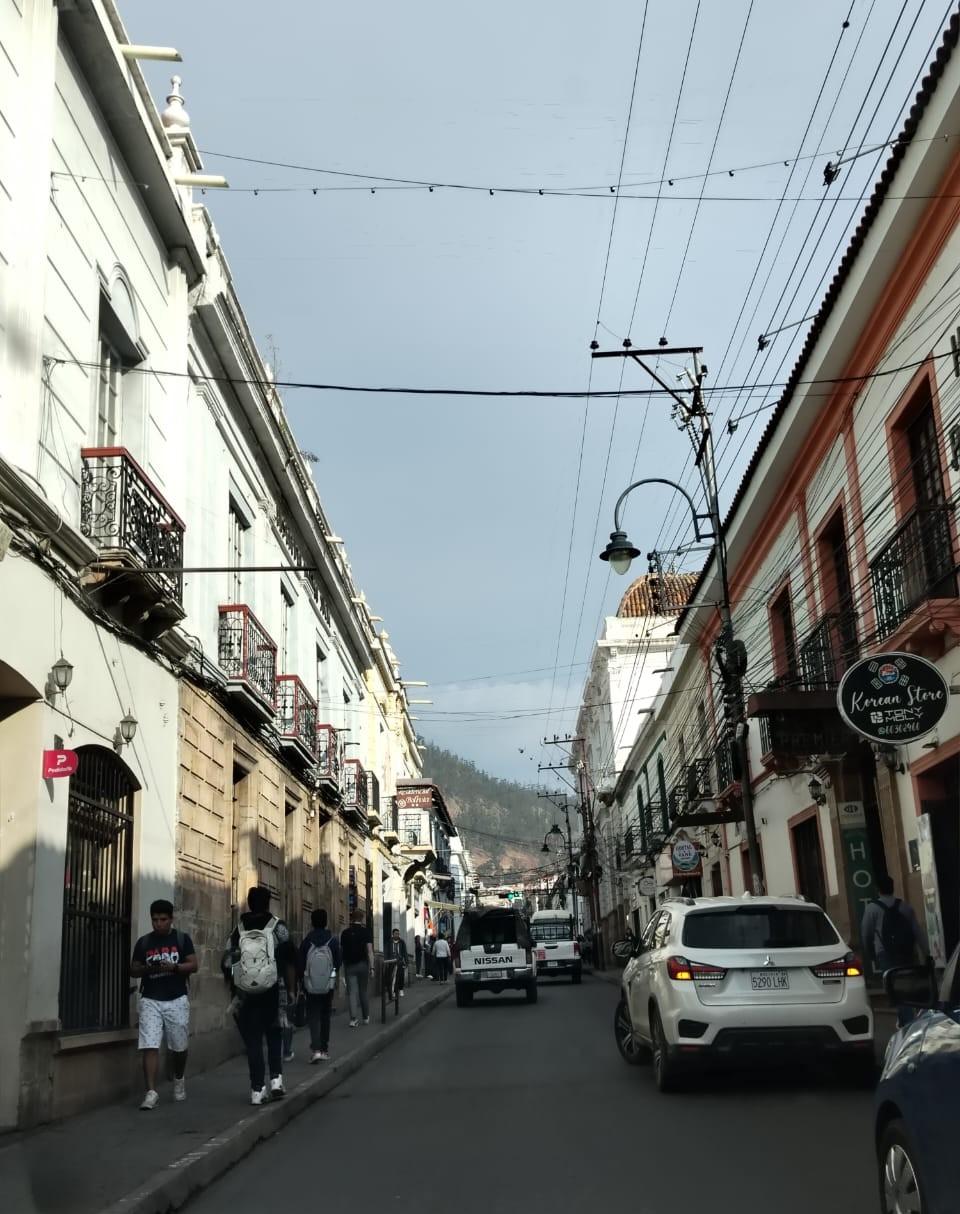 Calle inclinada y estrecha con vehículos y peatones en el centro colonial de Sucre